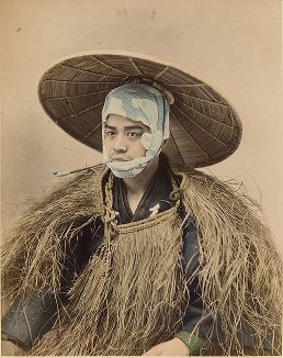 Курильщик в соломенном плаще, в платке и дорожной соломенной шляпе. Крашенная вручную японская альбуминовая фотография эпохи Мэйдзи (1868-1912). 